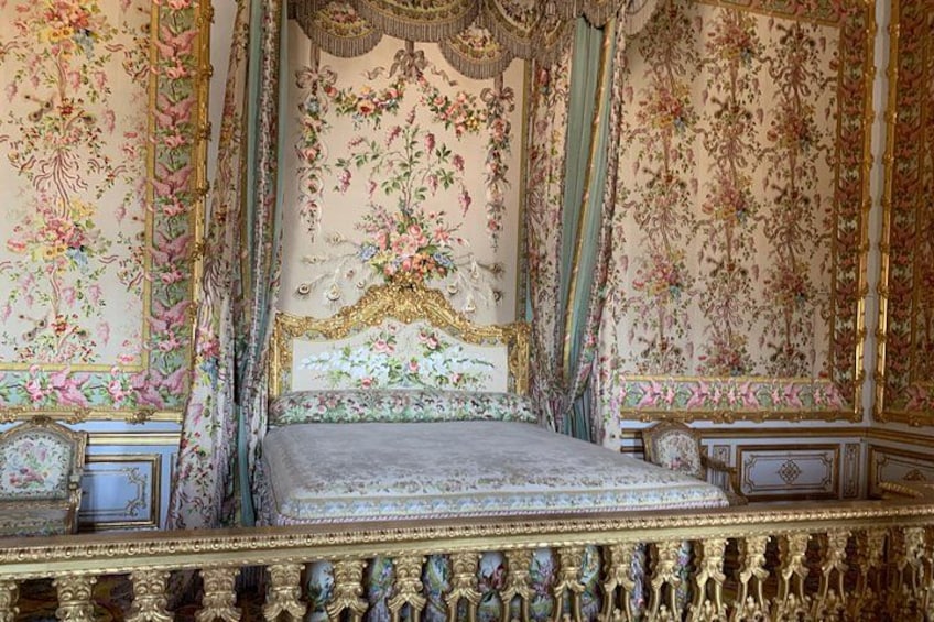 Una cama ornamentada con papel tapiz floral, detalles dorados y un dosel. 4