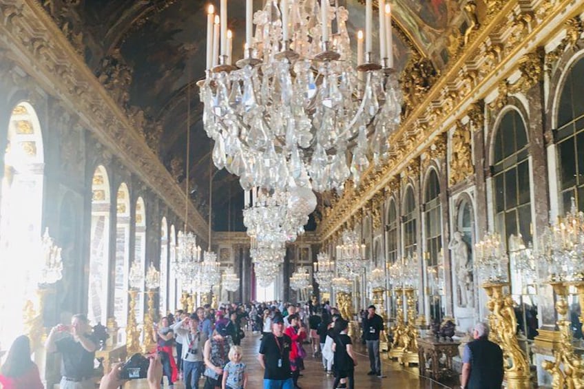 Un salón imponente con candelabros ornamentados, detalles dorados y una multitud de visitantes. 1