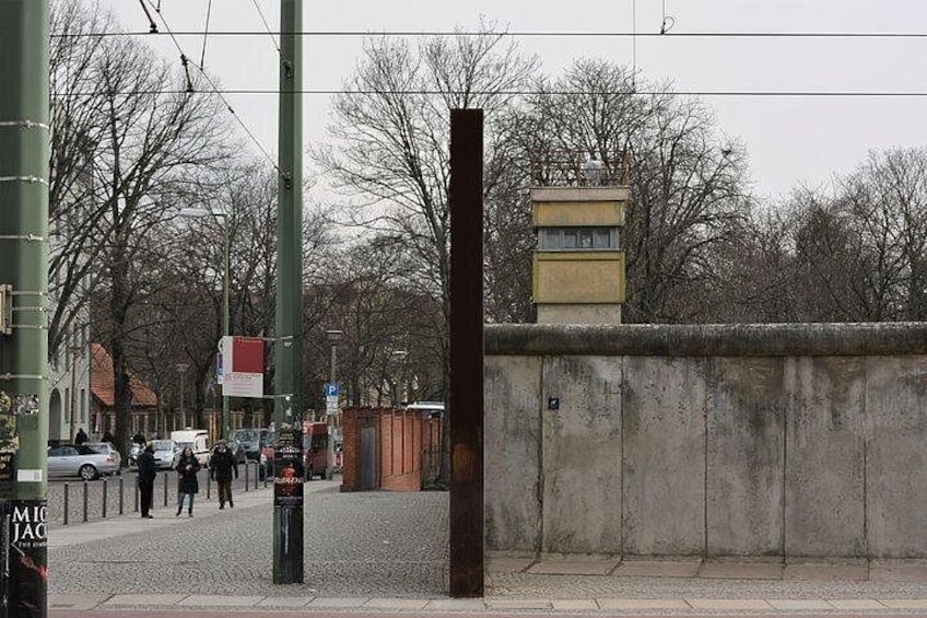 Una calle urbana con un muro de concreto, vías de tranvía y una parada de tranvía. 3