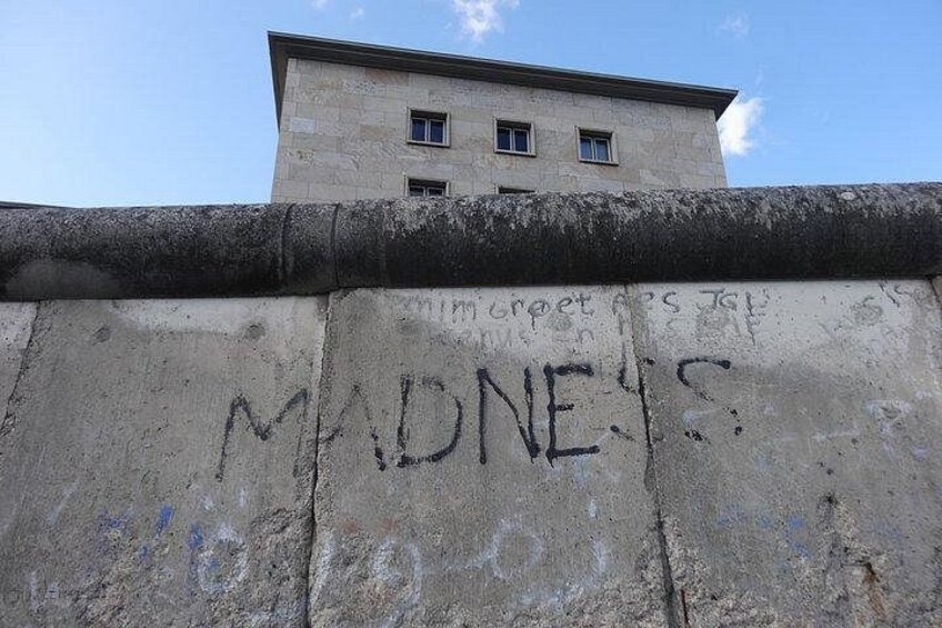 Un muro de concreto con grafitis, un edificio al fondo y un cielo despejado. 5