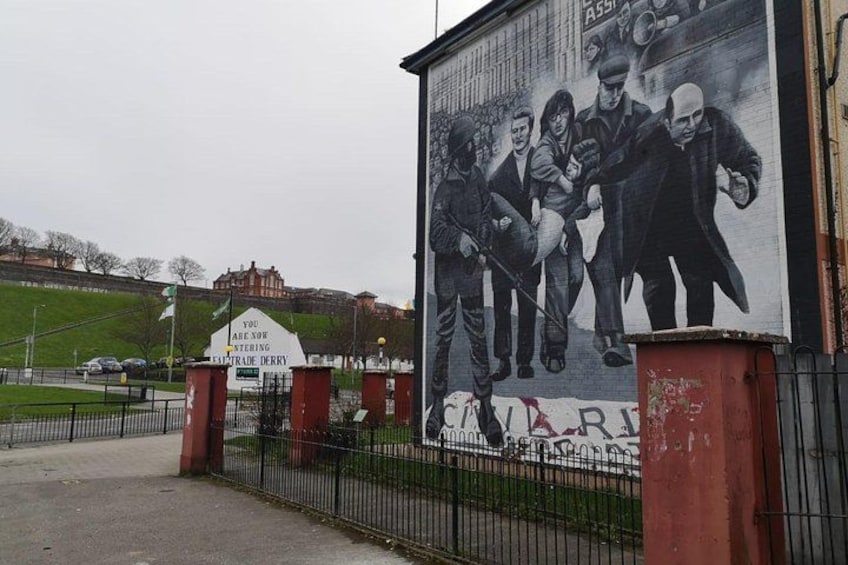 A mural of men on a wall, a sign that says "You are not entering", and a fence. 1