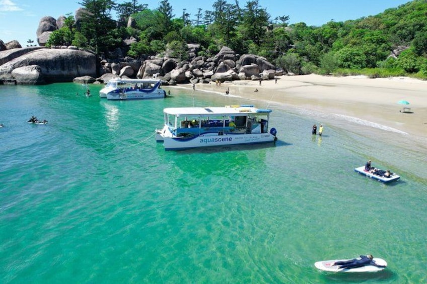 A boat named 'aquascene' on clear turquoise water, a sandy beach, and large rocks in the background. 4