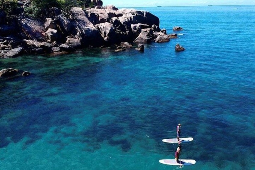 A person paddleboarding on clear blue water near rocky shores. 3