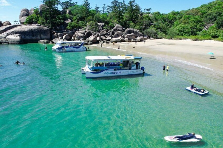 A boat named 'aquascene' on clear turquoise water, a sandy beach, and large rocks in the background. 3