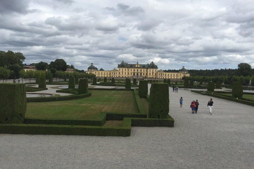 A formal garden with trimmed hedges, a large building in the background, and a cloudy sky. 2
