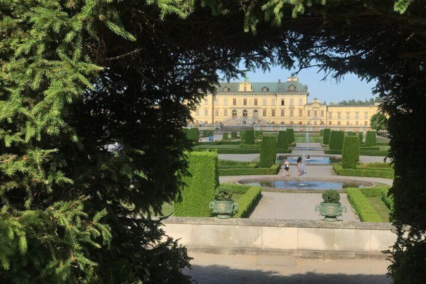 A formal garden with geometrically trimmed hedges, a central fountain, and a large building in the background. 4