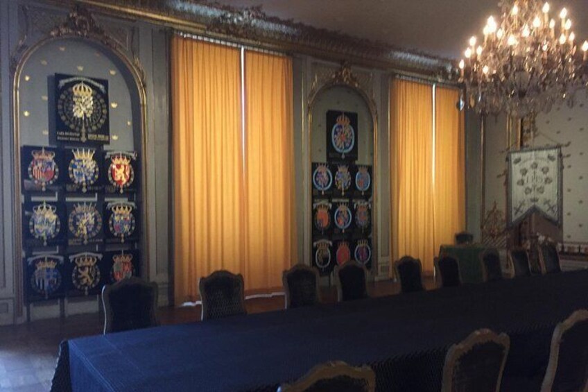 A formal room with a long table, chairs, and a chandelier. There are two walls decorated with framed items. 5