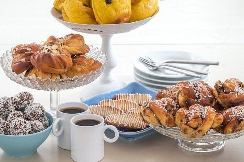 Et udvalg af kager og bagværk, herunder en stand med gule donuts, en tallerken med kanelsnegle og en skål med chokoladeovertrukne kager. 2