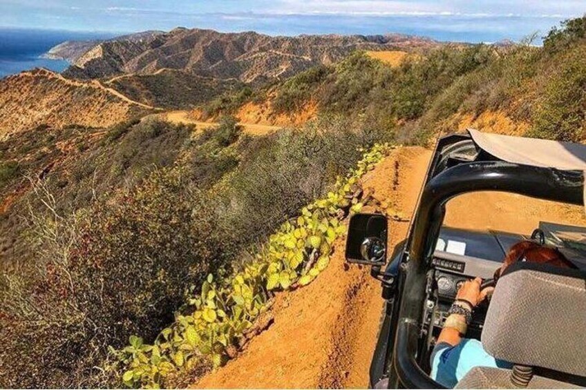 A vehicle on a dirt road surrounded by dry vegetation and hills. 4