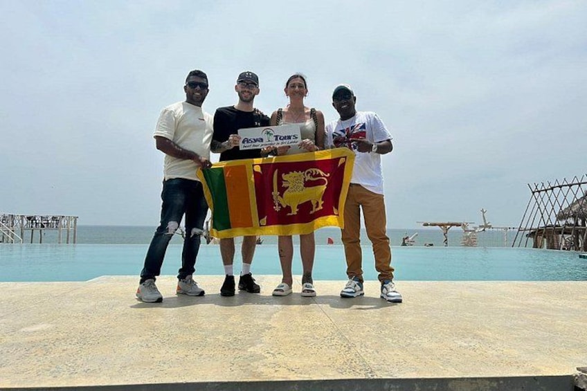 Un groupe de personnes brandissant un drapeau orné d’un emblème représentant un lion, debout sur une plateforme en béton, près d’une étendue d’eau, avec une jetée en arrière-plan. 5