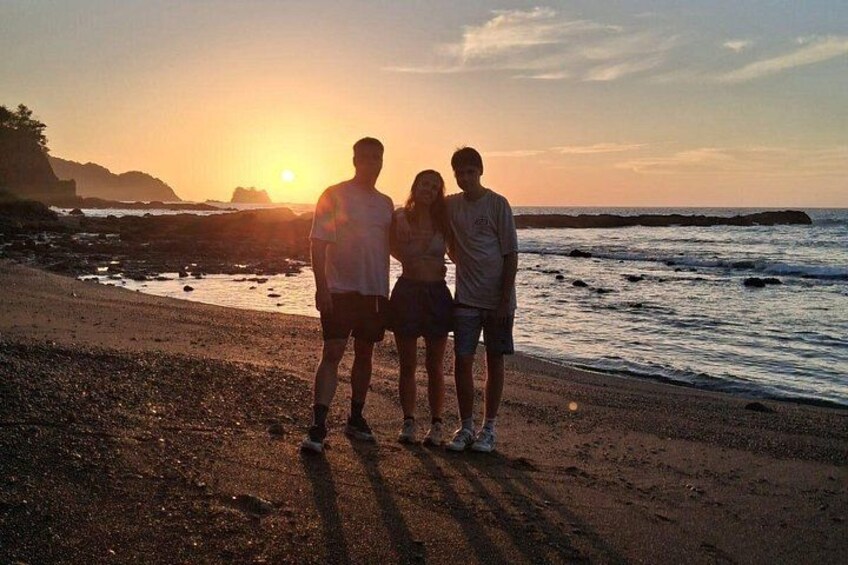 Three people standing on a beach at sunset with the sun setting over the ocean. 3
