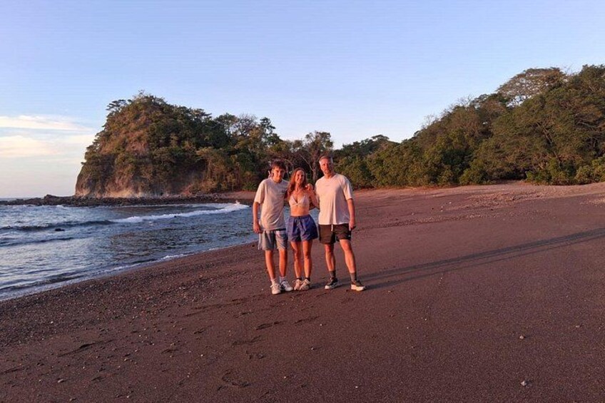 Three people standing on a beach with a rocky cliff in the background. 5