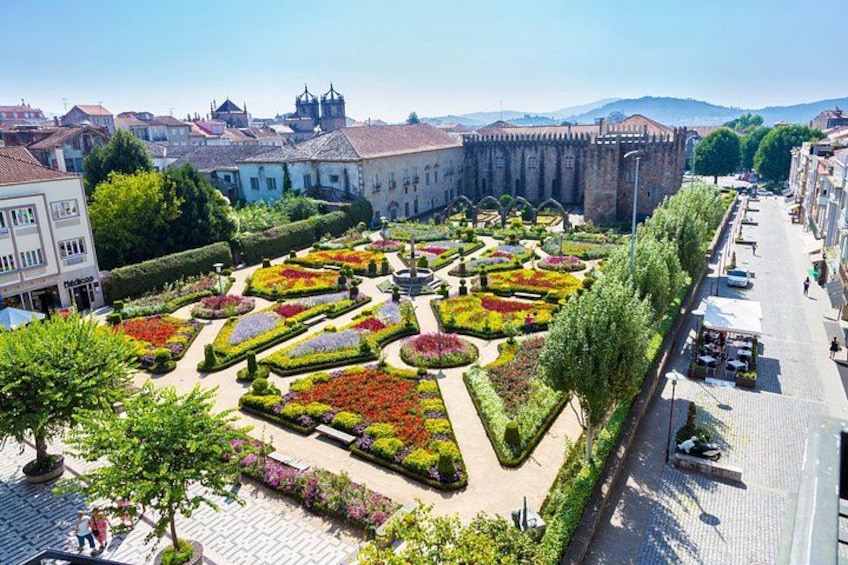 A historic square with ornate gardens, a prominent building with a tower, and a cobblestone street. 3