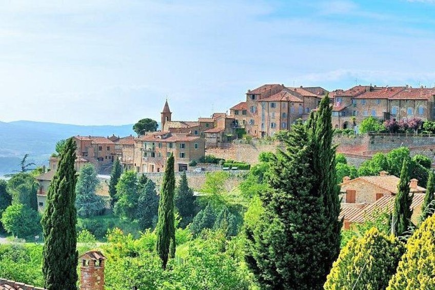 A hillside village with terracotta-roofed buildings, cypress trees, and a clear sky. 2