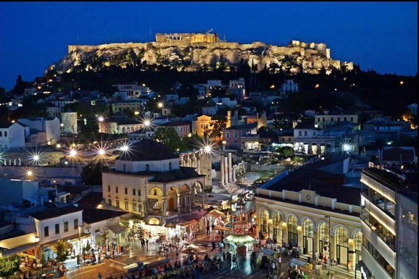 A cityscape at night with a prominent hilltop fortress, illuminated buildings, and a bustling street below. 3