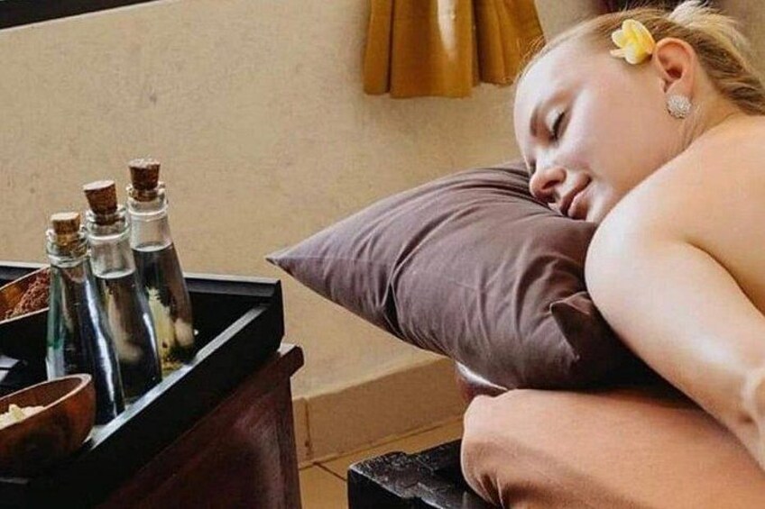 Una persona descansando en una cama con un almohadón, una bandeja con botellas y una ventana con cortinas. 5