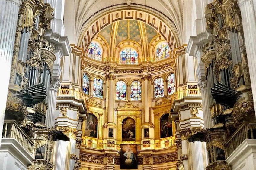 An ornate church interior with stained glass windows, gold detailing, and classical columns. 1
