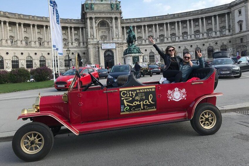 En ældre rød bil med et skilt, der siger 'City of Royal Cares Tours', parkeret foran en stor, udsmykket bygning. 5
