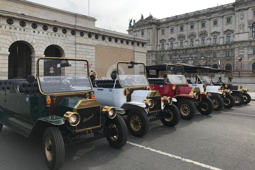 Une rangée de voitures anciennes est garée devant un bâtiment doté d’arcades et d’une façade de style classique. 3