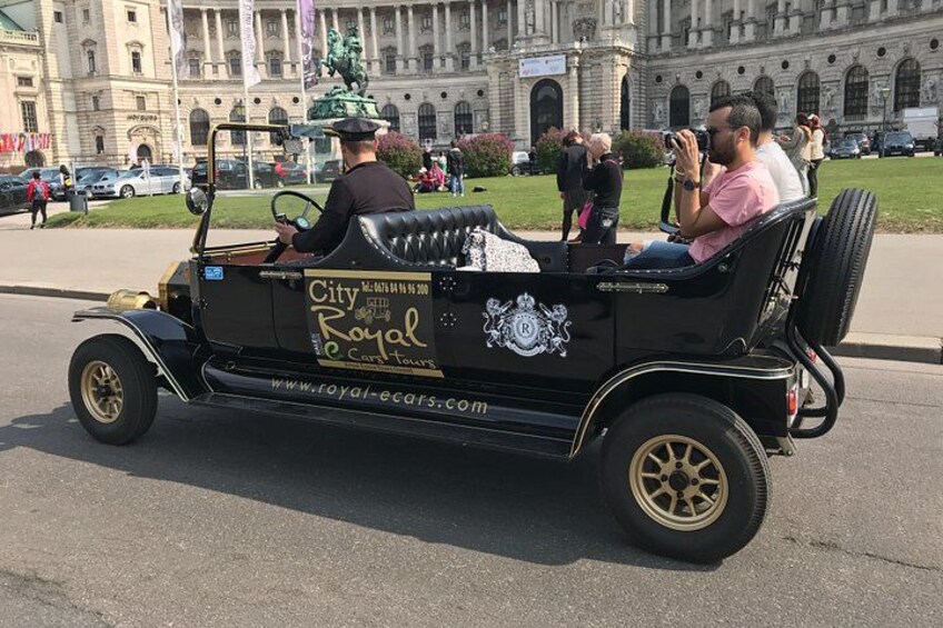 En klassisk bil med teksten 'City Royal Car Tours' parkeret foran en stor bygning med søjler. 2
