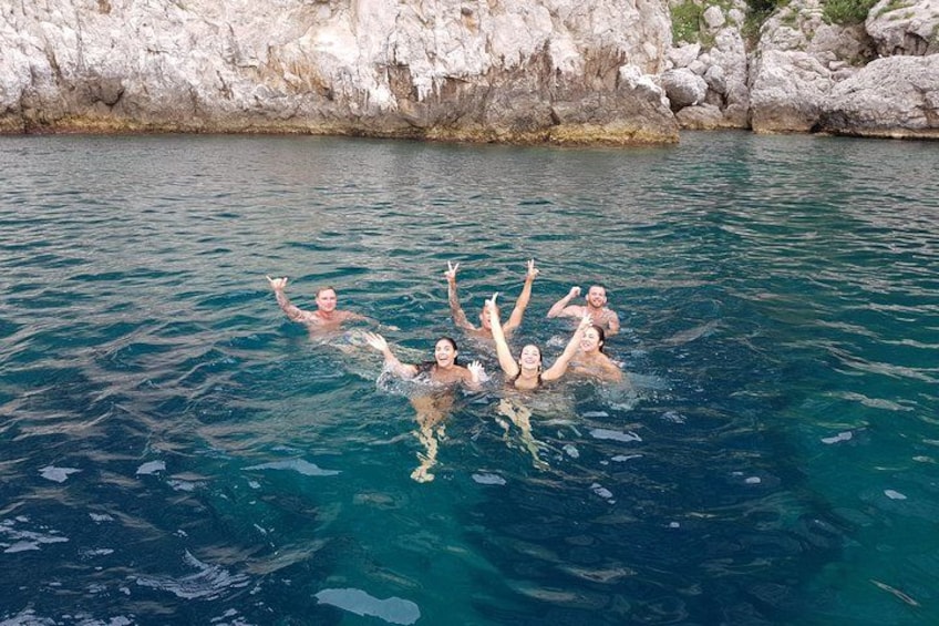 Persone che nuotano in un mare cristallino con alte scogliere sullo sfondo. 5