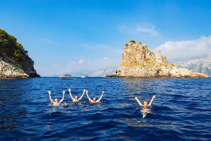 Un groupe de personnes nage dans la mer, avec une île rocheuse et des bateaux en arrière-plan. 5