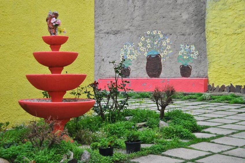 A red tiered fountain, a yellow wall, and a mural with potted plants. 3