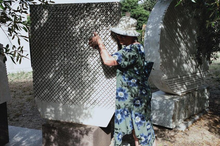 A person in a floral dress and hat interacting with a large, metallic structure outdoors. 2