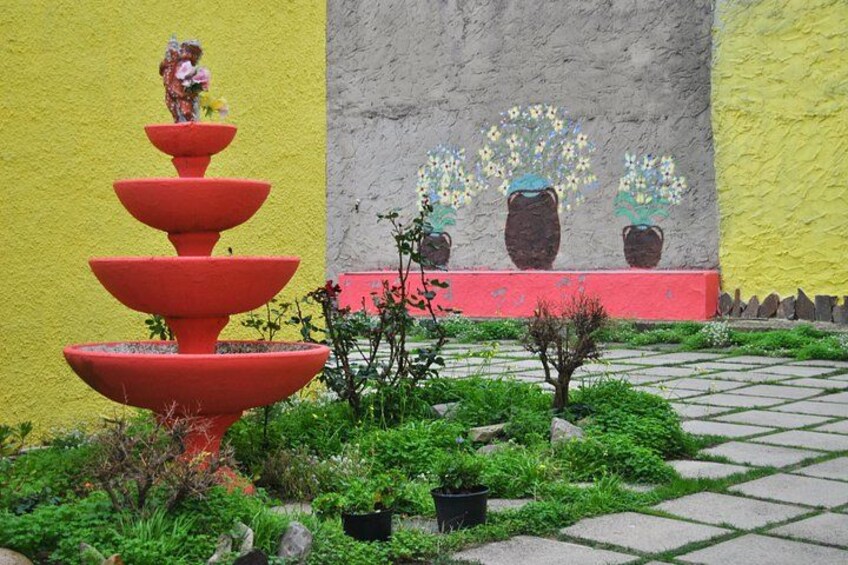 Une fontaine rouge à étages, un mur jaune et une fresque ornée de plantes en pot. 3