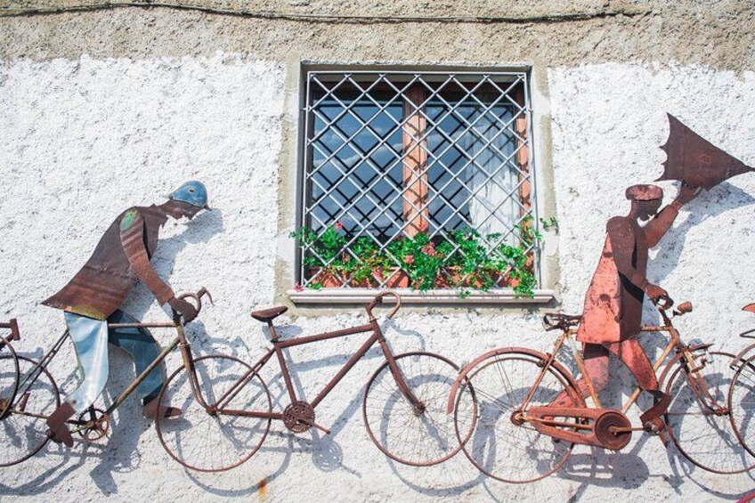 A white wall with a window, two bicycles, and two metal sculptures of figures. 1