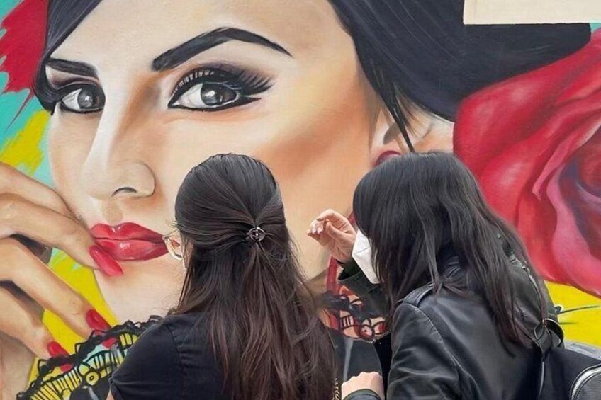 A mural with a woman's face, a red rose, and two people observing it. 3