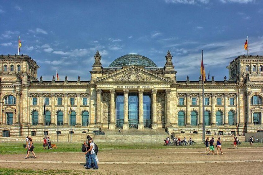 Un gran edificio histórico con una cúpula y columnas, rodeado de un campo de béisbol donde juegan personas. 1