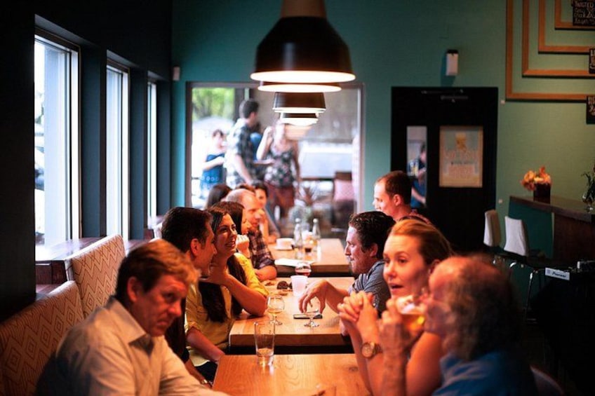 Un grupo de personas cenando en un restaurante con un amplio ventanal y una lámpara colgante. 3