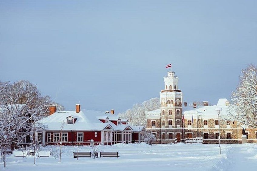 A snow-covered building with a tower, surrounded by trees and a bench. 5