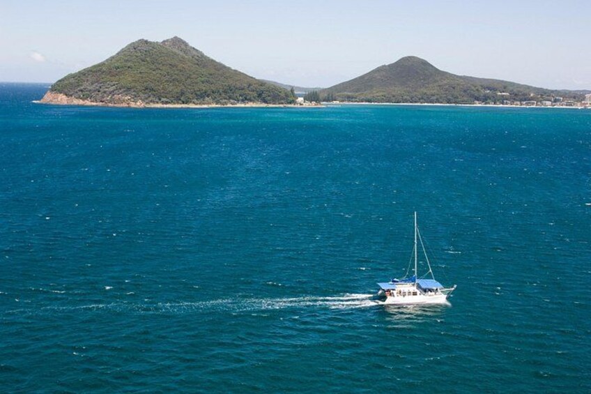 A sailboat on turquoise waters with two green hills in the background. 4