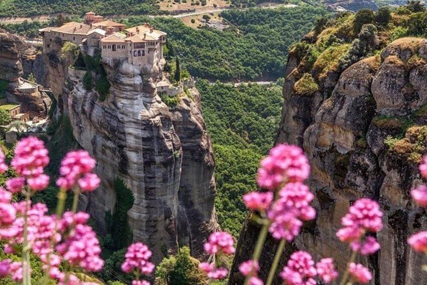A cliffside monastery with a village, surrounded by greenery and pink flowers. 4