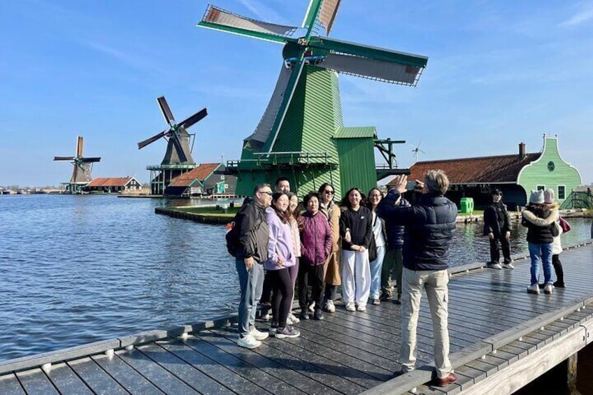 A group of people on a wooden dock by windmills and water. 1