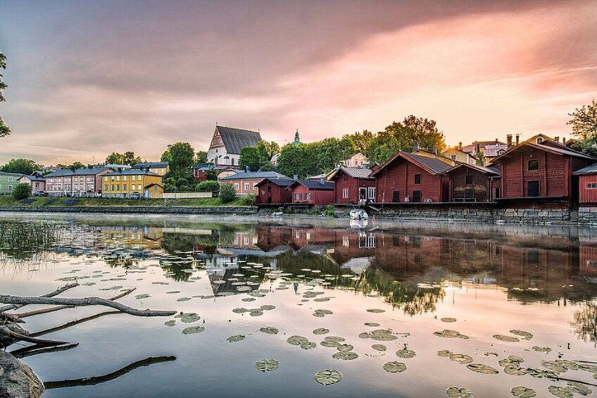 A calm river with reflections of buildings, lily pads, and a cloudy sky. 2