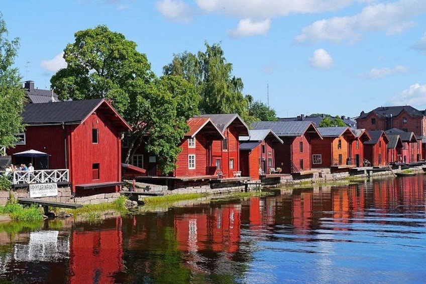 A row of red wooden houses by a calm water body, with a clear sky above. 1