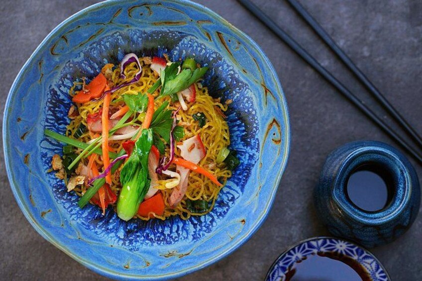 Un tazón de fideos con verduras y un tazón pequeño de salsa de soja. 3