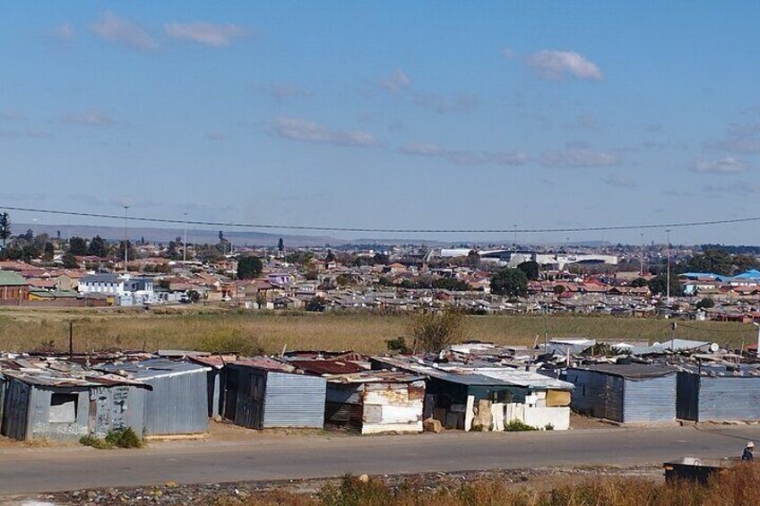 A rural settlement with makeshift housing and a distant view of a larger town. 1
