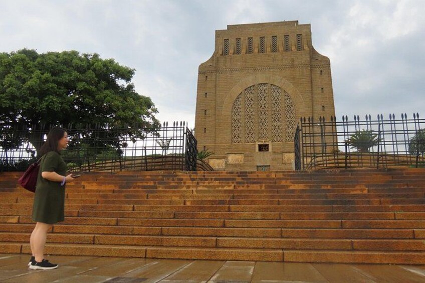 A person standing on steps in front of a large, arched building with a fence in the background. 3