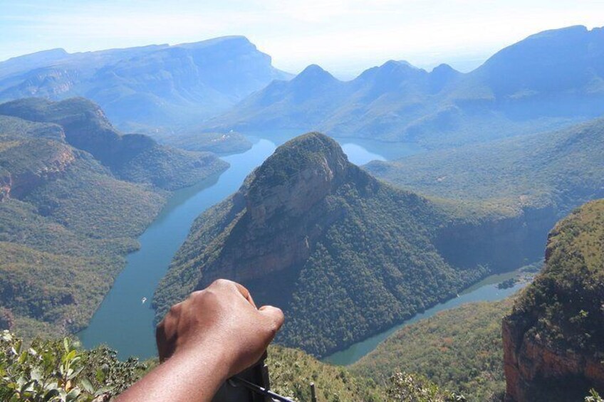 A hand holding a camera, overlooking a valley with a river and mountains. 4