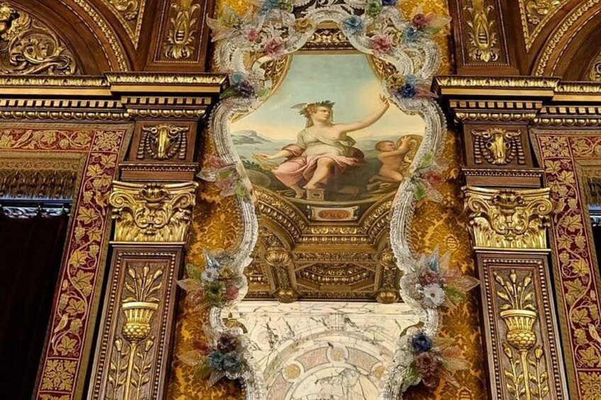 An ornate ceiling with a central painting of a woman, surrounded by elaborate gold and floral decorations. 4