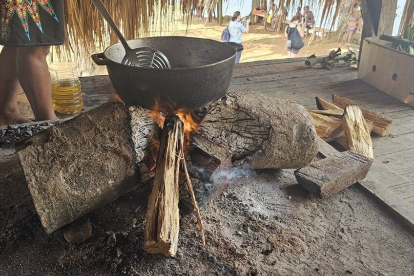 Escena de cocina con un wok sobre fuego abierto, leña y una persona cerca. 4