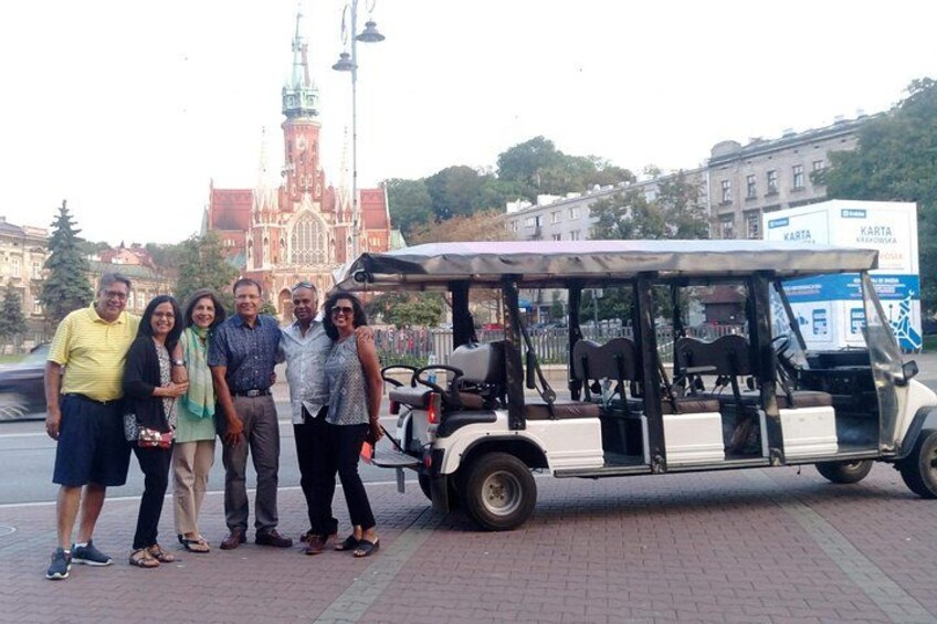 A group of people standing in front of a white and brown trolley, with a large red and white building in the background. 4