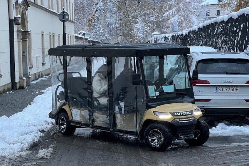 A covered vehicle with a driver, parked on a snow-covered street. 2