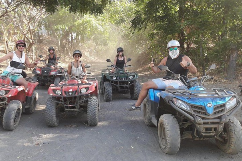 Four people riding ATVs on a dirt road surrounded by trees. 3