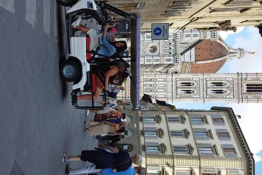 A white tour bus with passengers, a large clock tower, and a building with a dome in the background. 2