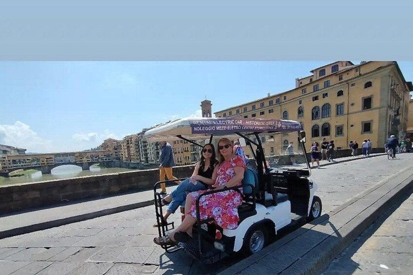 A couple sitting in a golf cart on a waterfront promenade with buildings in the background. 4